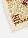 Close-up of the Ecru Acapulco Weave Kingsman Neckerchief on a white surface. The weave has a pattern with brown and gold colors. The words 'Peace Love Soul Hotel Dea' are visible.