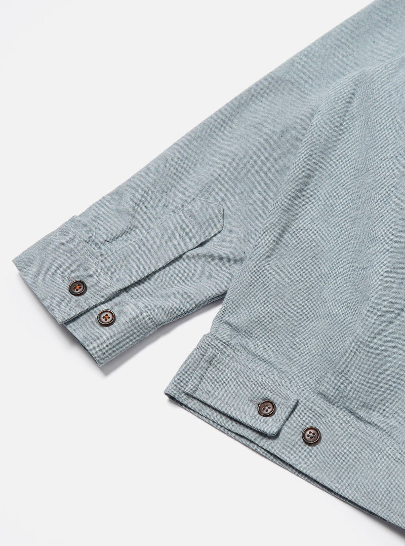 Close-up of the Indigo Reworked Jean Cloth Rose Bowl Jacket sleeve on a white surface. Light blue denim with brown buttons.