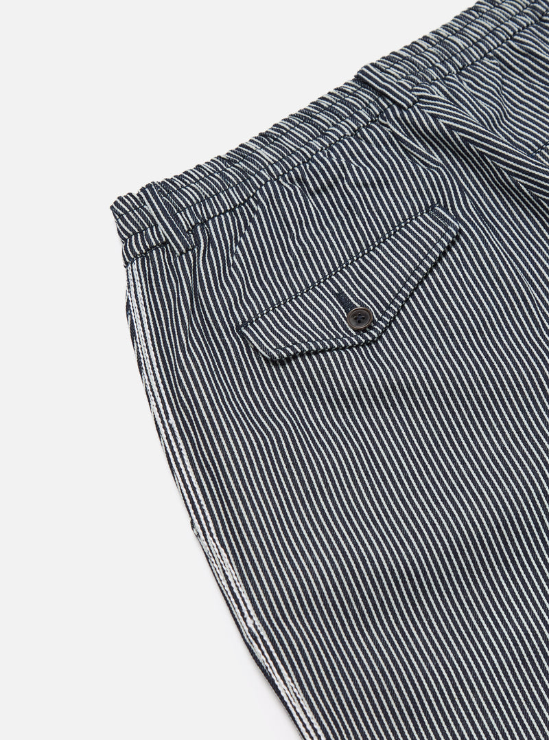 Close-up of Indigo Hickory Stripe Denim Pleated Track Pant on white. Features include striped denim, pleated design, and a small pocket. 