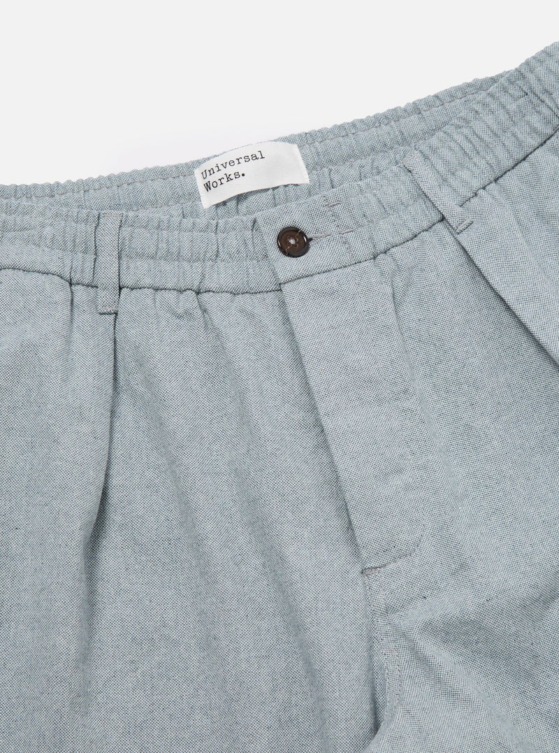 Close-up of the Indigo Reworked Jean Cloth Oxford Pant in light blue. Features an elastic waistband, button closure, and pleated design. Shot on a white background.