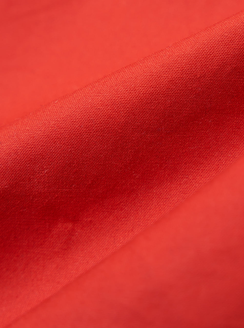 Close-up of the Orange British Wax Cotton Boston Parka fabric. The durable material is displayed on a plain background, highlighting the texture and vibrant color.