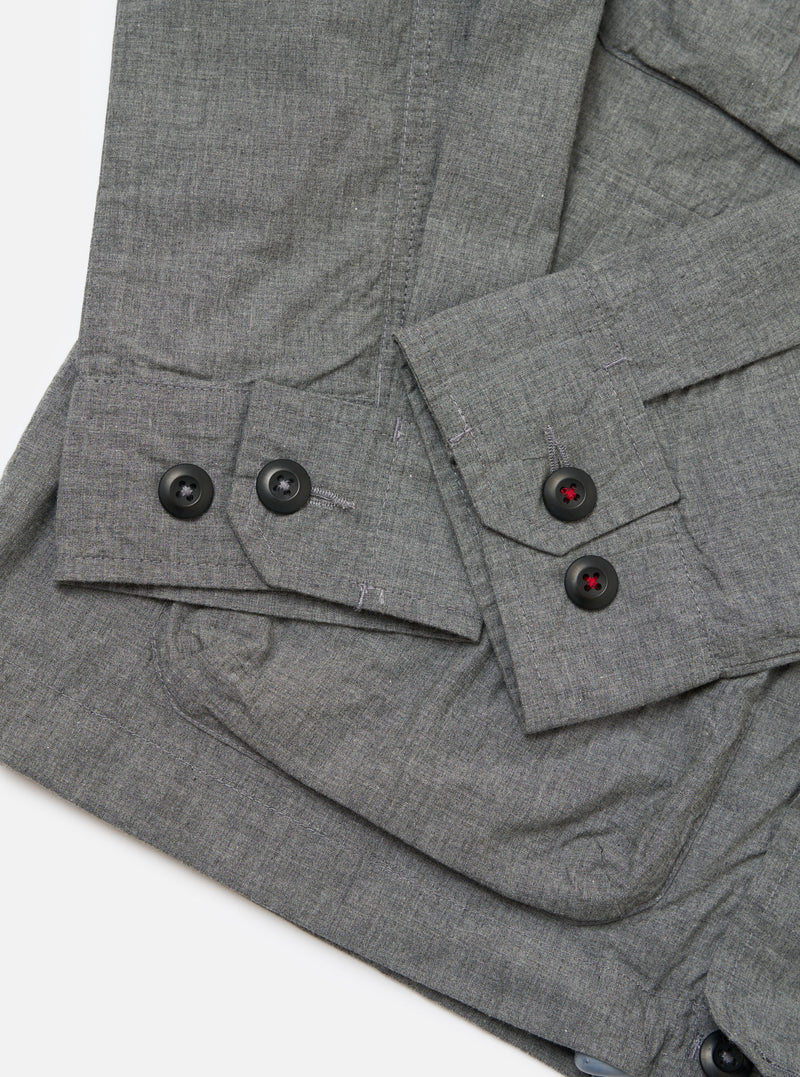Close-up of the Charcoal Organic Chambray Parachute Field Jacket on a white surface. The jacket features black buttons with red stitching. The chambray material has a subtle texture.