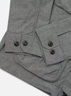 Close-up of the Charcoal Organic Chambray Parachute Field Jacket on a white surface. The jacket features black buttons with red stitching. The chambray material has a subtle texture.