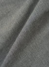 Close-up of the Charcoal Organic Chambray Parachute Field Jacket fabric. The charcoal-colored material is folded, showing its texture. The background is a plain surface.