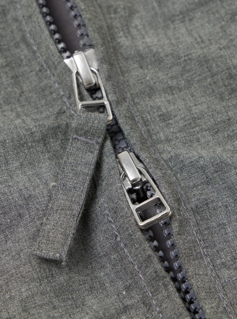 Close-up of the Charcoal Organic Chambray Parachute Liner Jacket. The image shows the zipper with a silver pull tab on the charcoal chambray fabric. 
