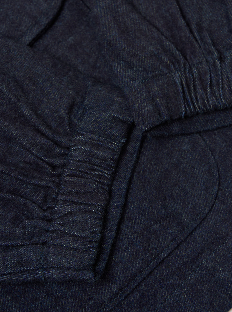 Close-up of the Indigo Brushed Denim Labour Jacket showing the dark blue denim material and pocket detail. The jacket is laid flat on a neutral surface.