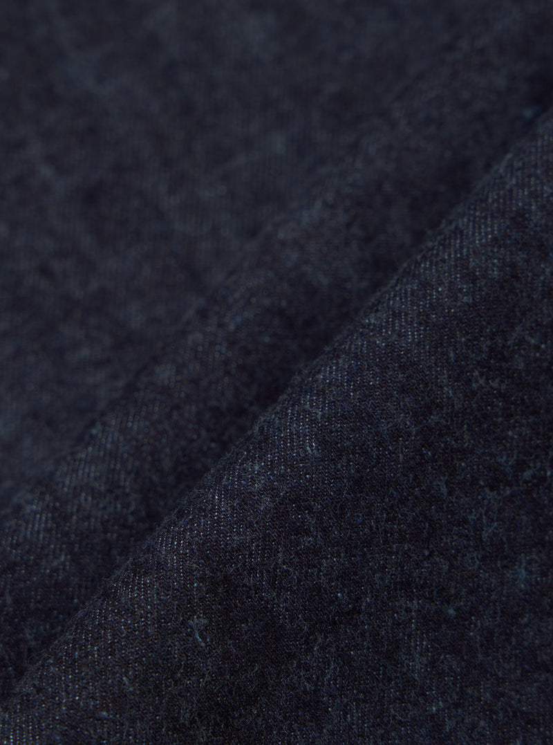 Close-up of the Indigo Brushed Denim Labour Jacket fabric. The brushed denim has a soft texture and rich indigo color. Shot on a simple background.