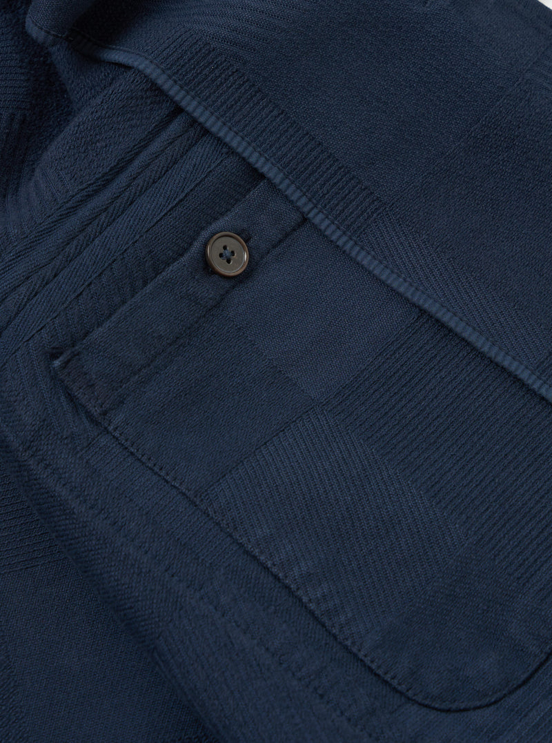 Close-up of the dark navy Patchwork Weave Cotton Labour Jacket, showing the textured weave, button detail, and pocket. Shot on a flat surface.