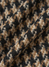 Close-up of the Sand Cortina Tweed Windcheater fabric. The tweed has a brown, black, and beige houndstooth pattern. The fabric is draped to show texture.