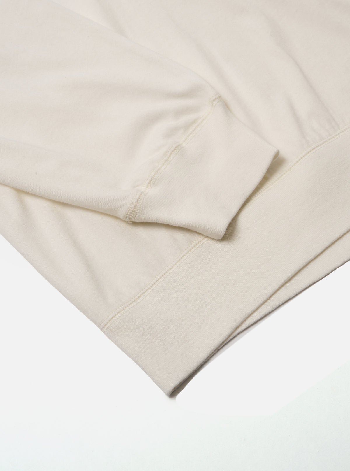 Close-up of the ecru Single Jersey Funnel Neck Tee sleeve. The soft, neutral-toned fabric is neatly folded on a clean white surface, highlighting the tee's texture and design.