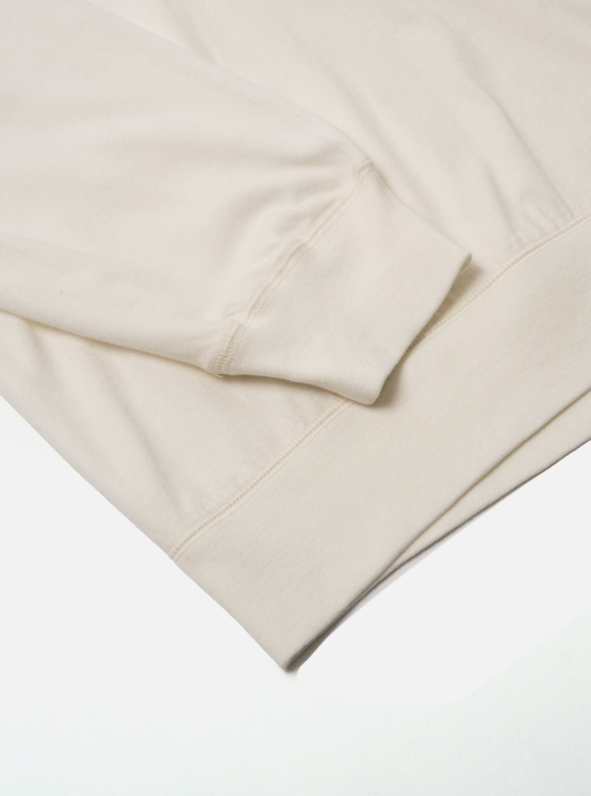 Close-up of the ecru Single Jersey Funnel Neck Tee sleeve. The soft, neutral-toned fabric is neatly folded on a clean white surface, highlighting the tee's texture and design.