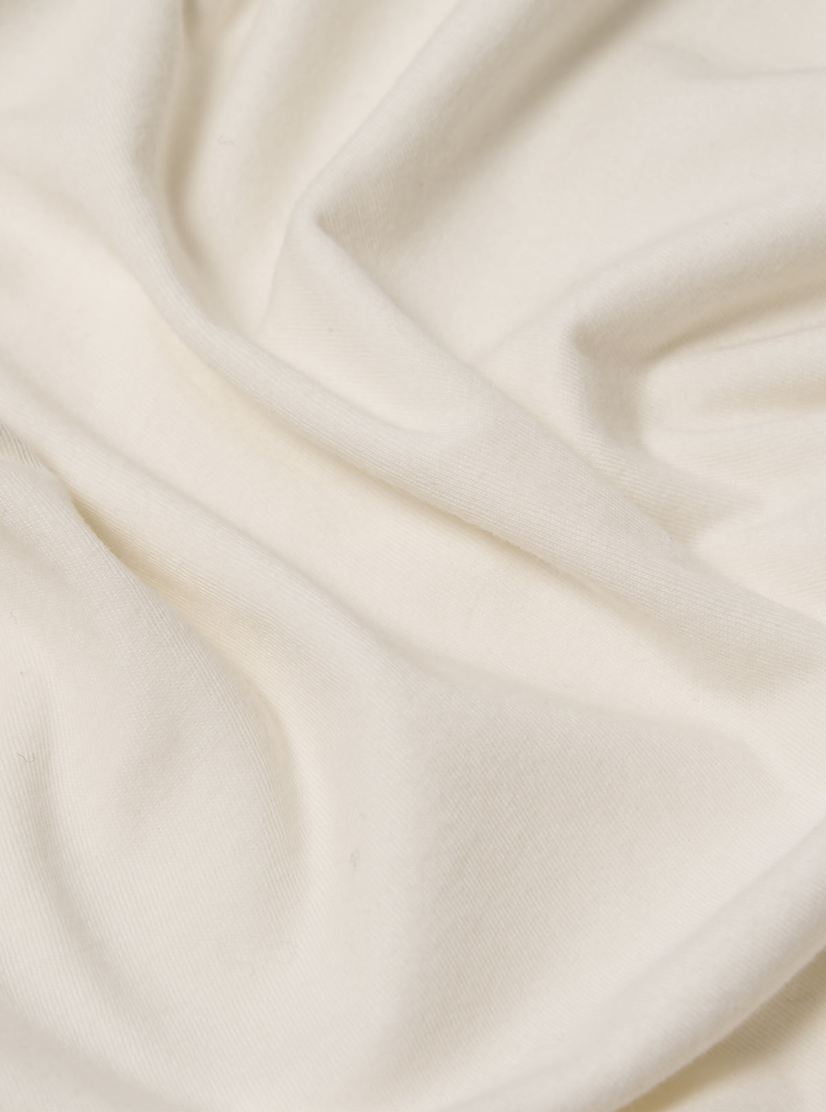 Close-up of the ecru Single Jersey Funnel Neck Tee fabric. The soft, single jersey material is draped on a plain surface, highlighting its texture and subtle ecru color.