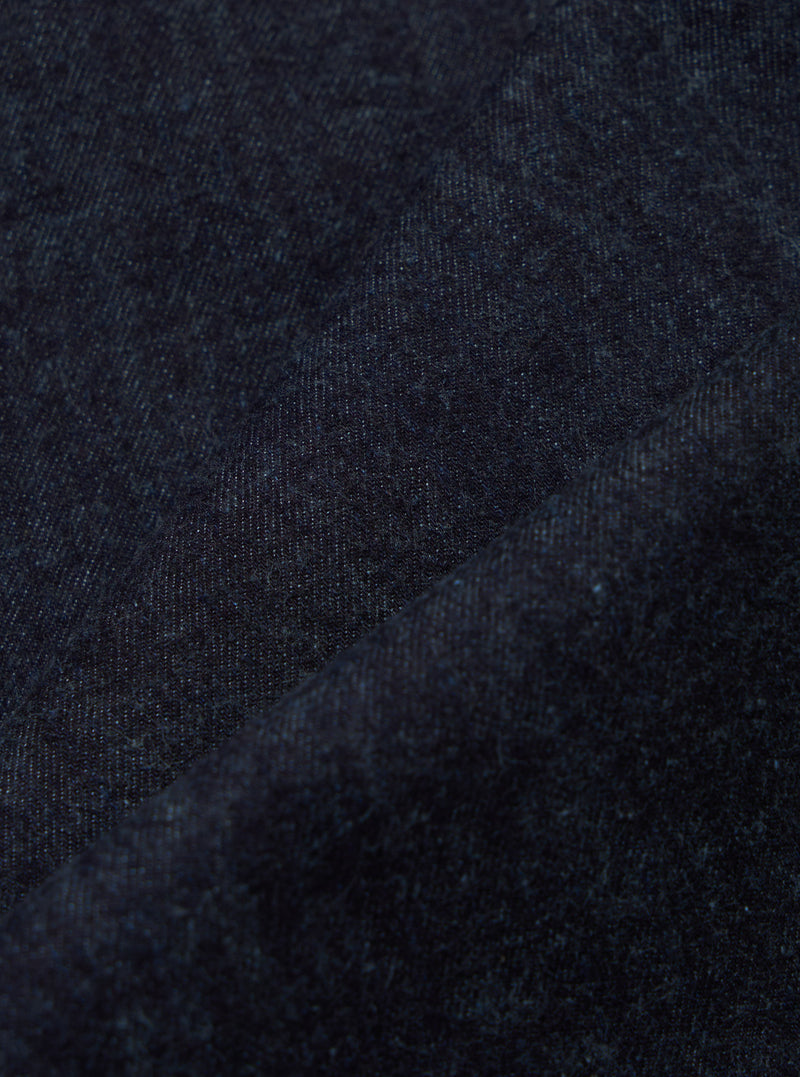 Close-up of indigo brushed denim military chino fabric. The dark blue material is textured and folded, showcasing its weave. Studio shot.