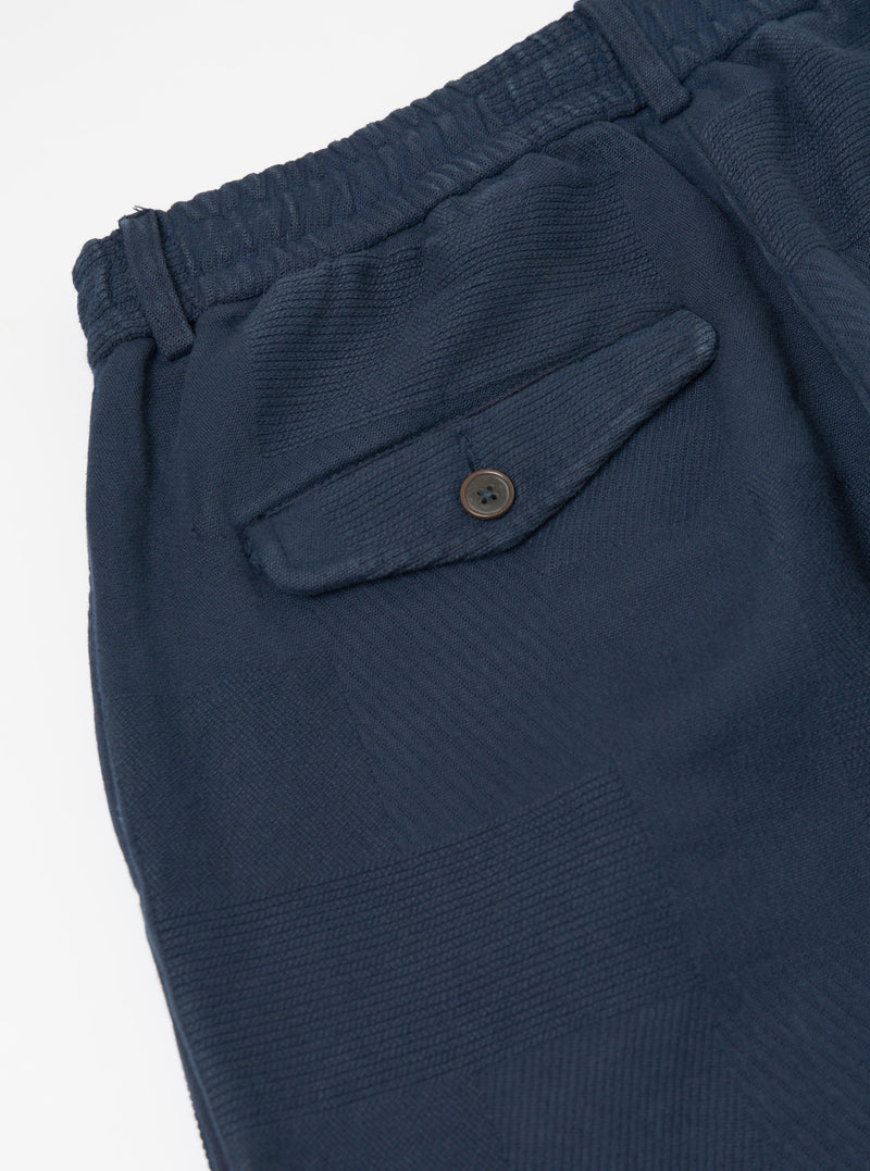 Close-up of the Dark Navy Patchwork Weave Cotton Pleated Track Pant on a white surface, showing the textured fabric and buttoned pocket.
