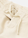 Close-up of the Ecru Patchwork Weave Cotton Pleated Track Pant on a white background. The ecru cotton has a textured, patchwork weave. Drawstring and button details are visible.