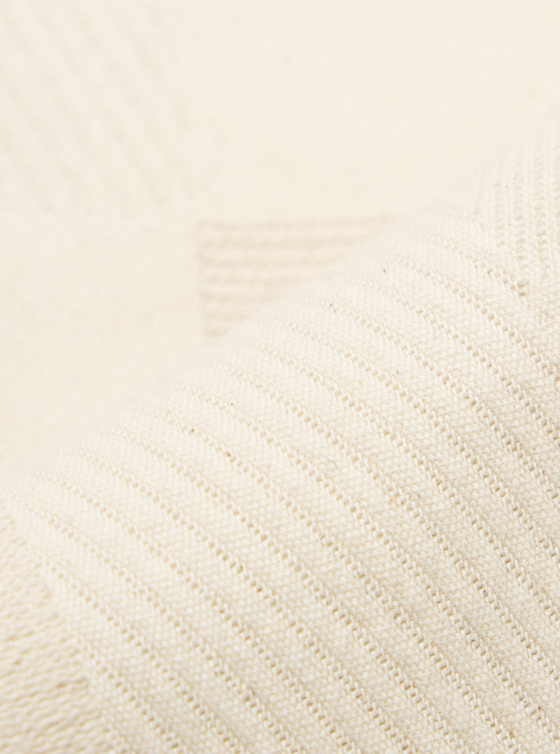 Close-up of the Ecru Patchwork Weave Cotton Pleated Track Pant fabric. The ecru cotton material is woven with a patchwork pattern and pleated texture, displayed on a flat surface.