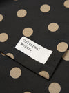 Close-up of a Black Bold Dot Print Rayon Evening Scarf. The scarf has tan dots on a black background. A white tag with "Universal Works" is sewn on.