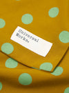 Close-up of a Mustard Bold Dot Print Rayon Evening Scarf. The scarf is mustard colored with light green polka dots. A white tag with "Universal Works." is sewn on.