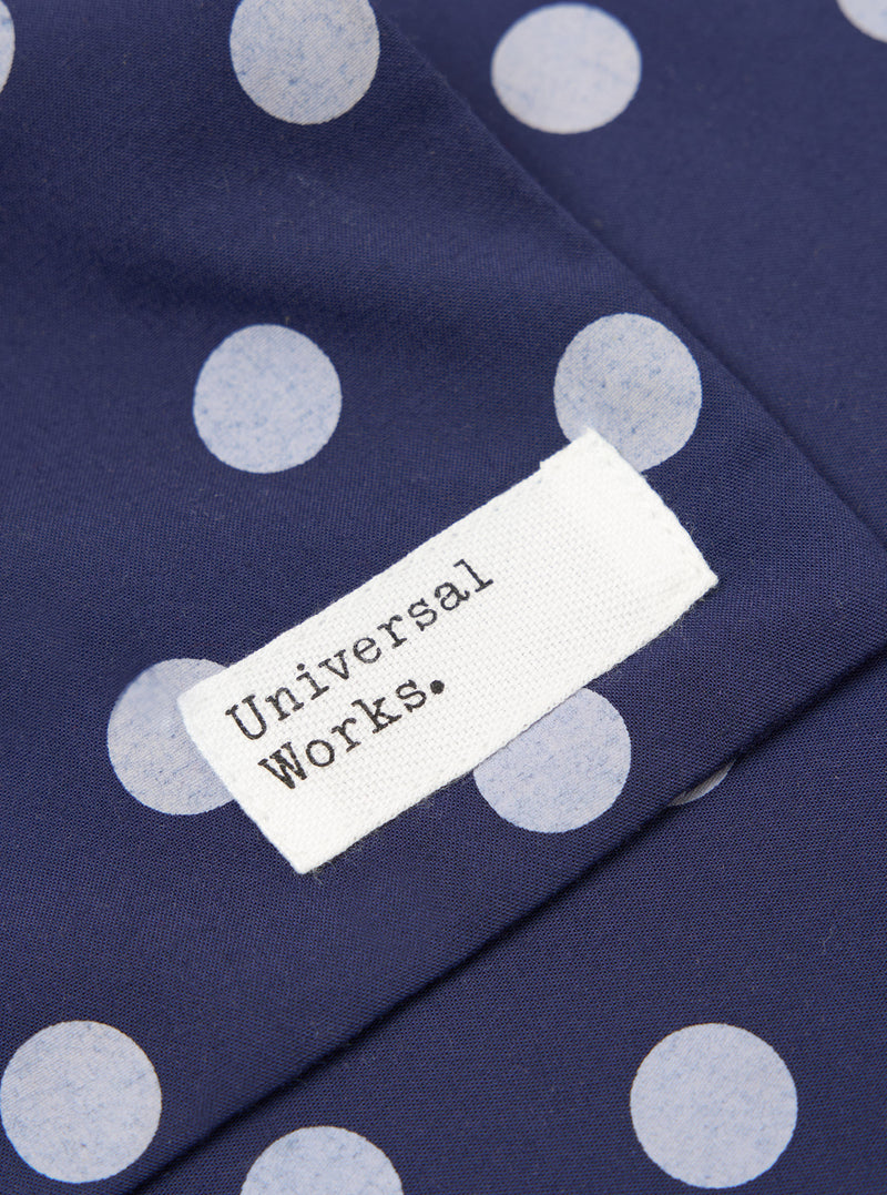 Close-up of the Navy Bold Dot Print Rayon Evening Scarf featuring a navy fabric with white polka dots and a white tag with the brand name 'Universal Works.'