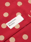 Close-up of a Red Bold Dot Print Rayon Evening Scarf. The scarf features a red background with tan polka dots and a white tag with black text. 