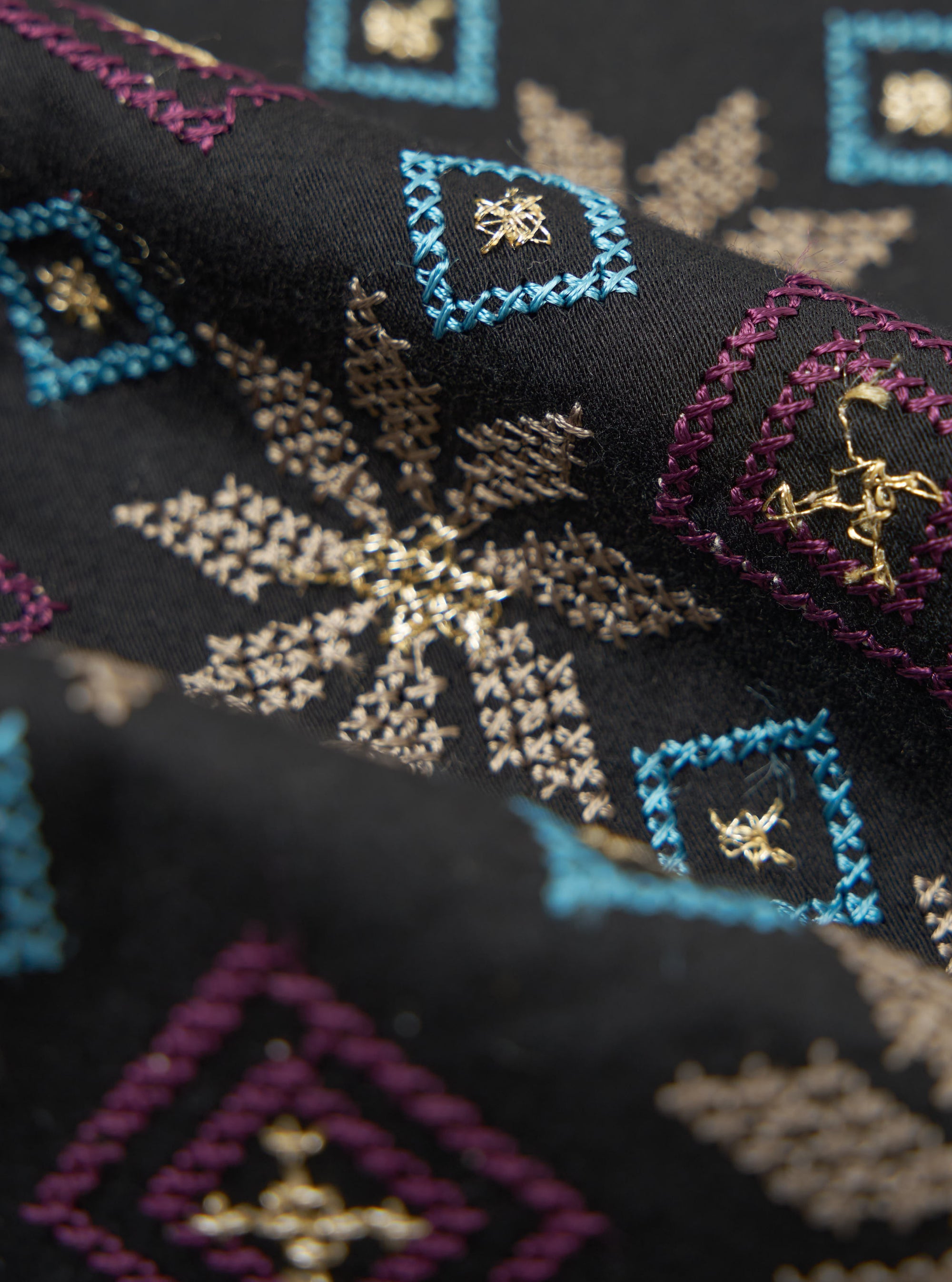 Close-up of a Black Embroidery Cotton Satin Embroidery Scarf. Features blue, purple, and gold embroidery on black satin. Shot with a shallow depth of field.