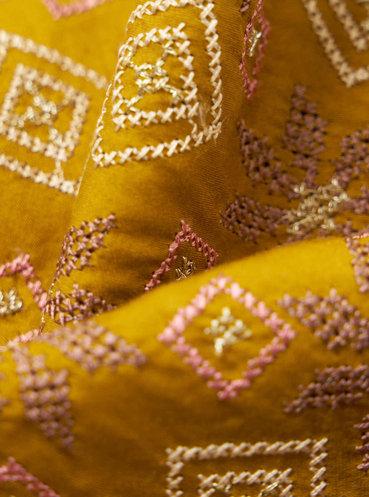 Close-up of the Mustard Embroidery Cotton Satin Embroidery Scarf. The mustard fabric features pink and white geometric embroidery. The scarf is draped on a dark background.