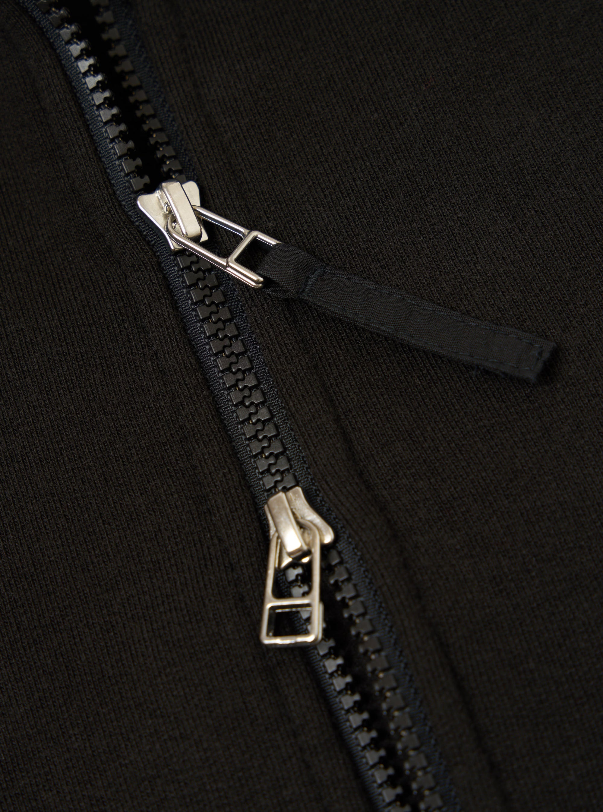 Close-up of the Black Brush Back Sweat Tyler Sweat Jacket, showcasing the zipper detail. The black fabric and silver zipper create a sleek contrast.