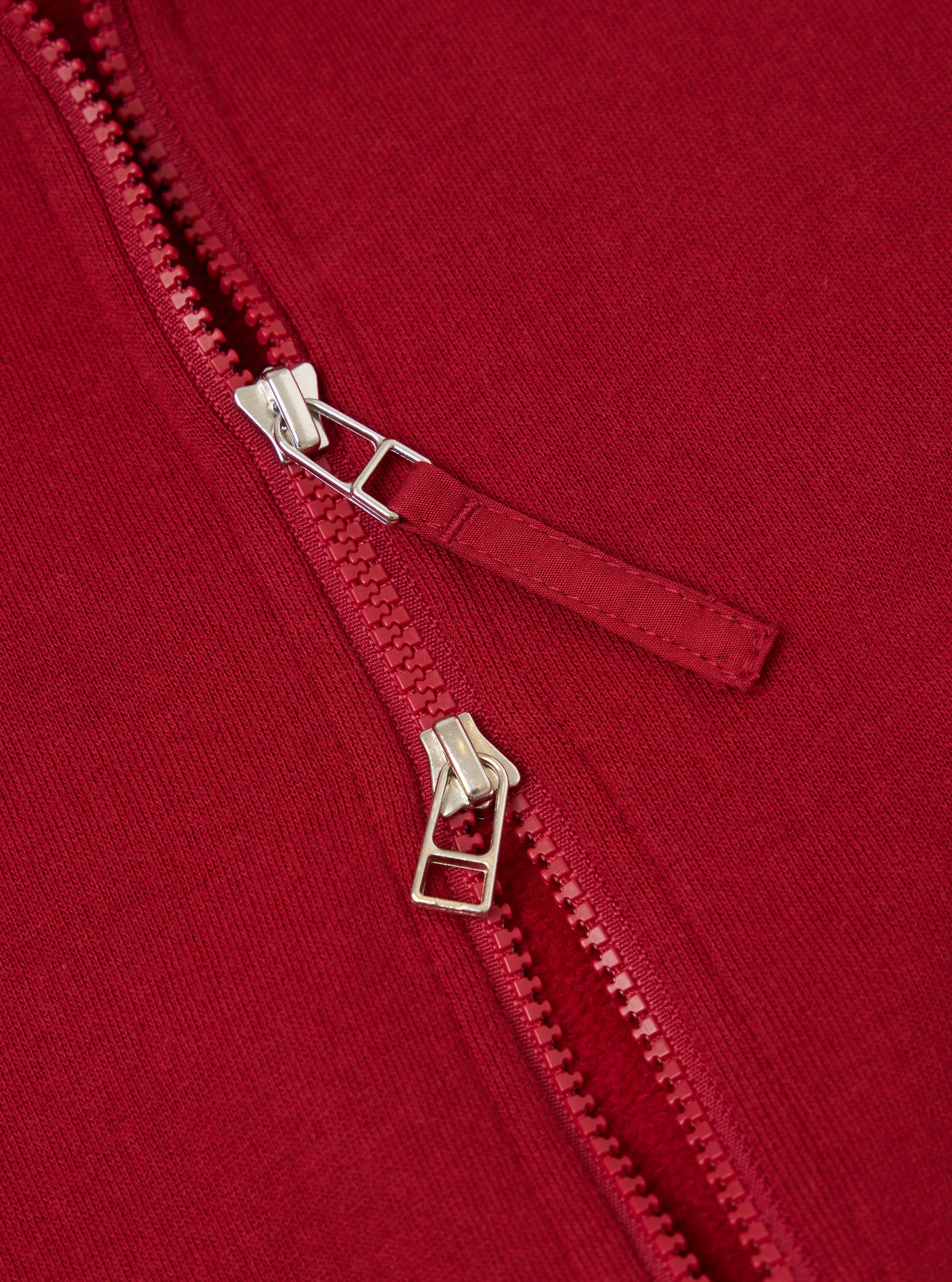 Close-up of the red Brush Back Sweat Tyler Sweat Jacket, showcasing the zipper detail and soft fabric texture. The image is tightly cropped, highlighting the jacket's quality.