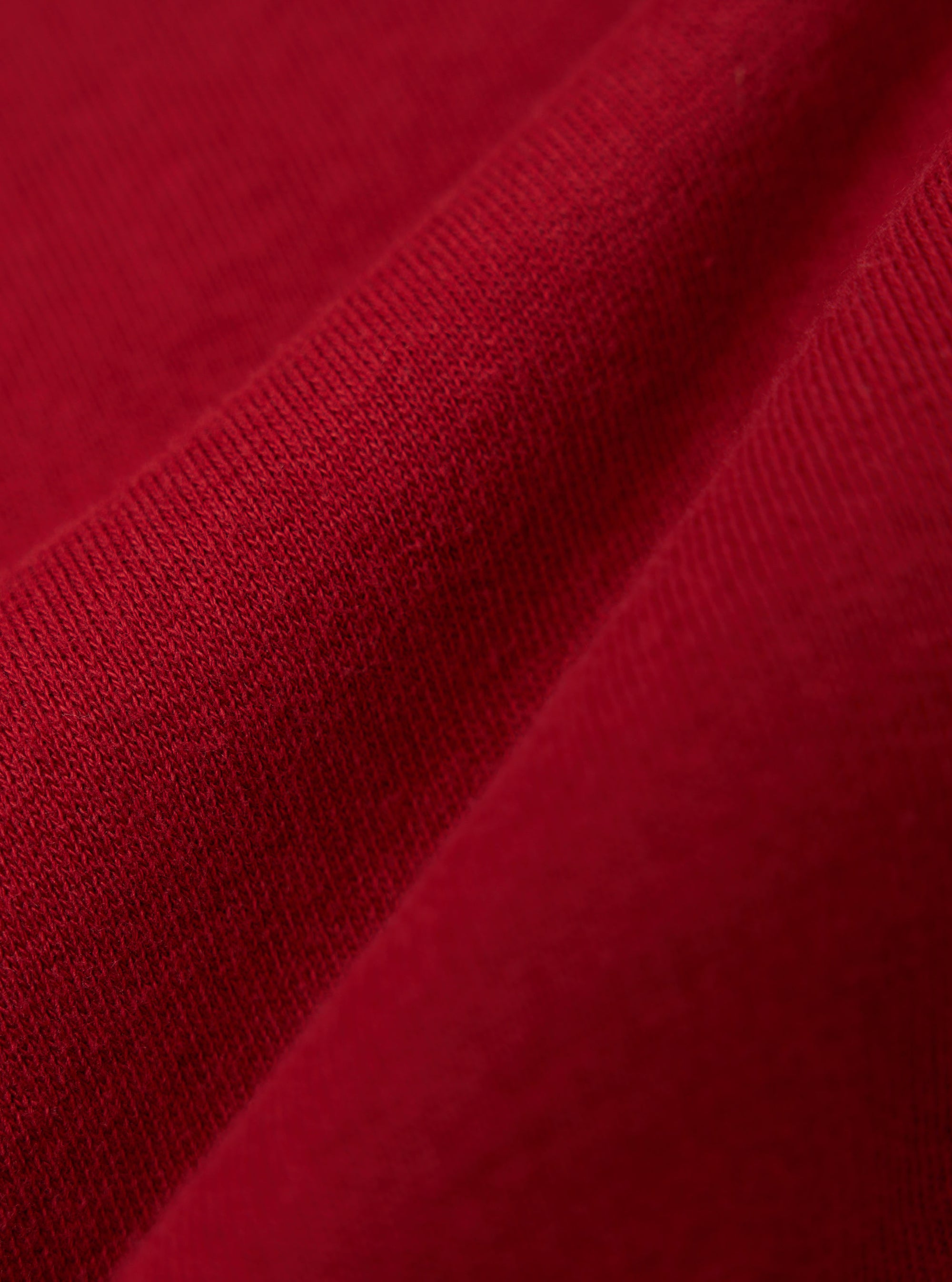 Close-up of the red fabric of the Red Brush Back Sweat Tyler Sweat Jacket, showing the texture and color. The jacket is casually draped on a flat surface.
