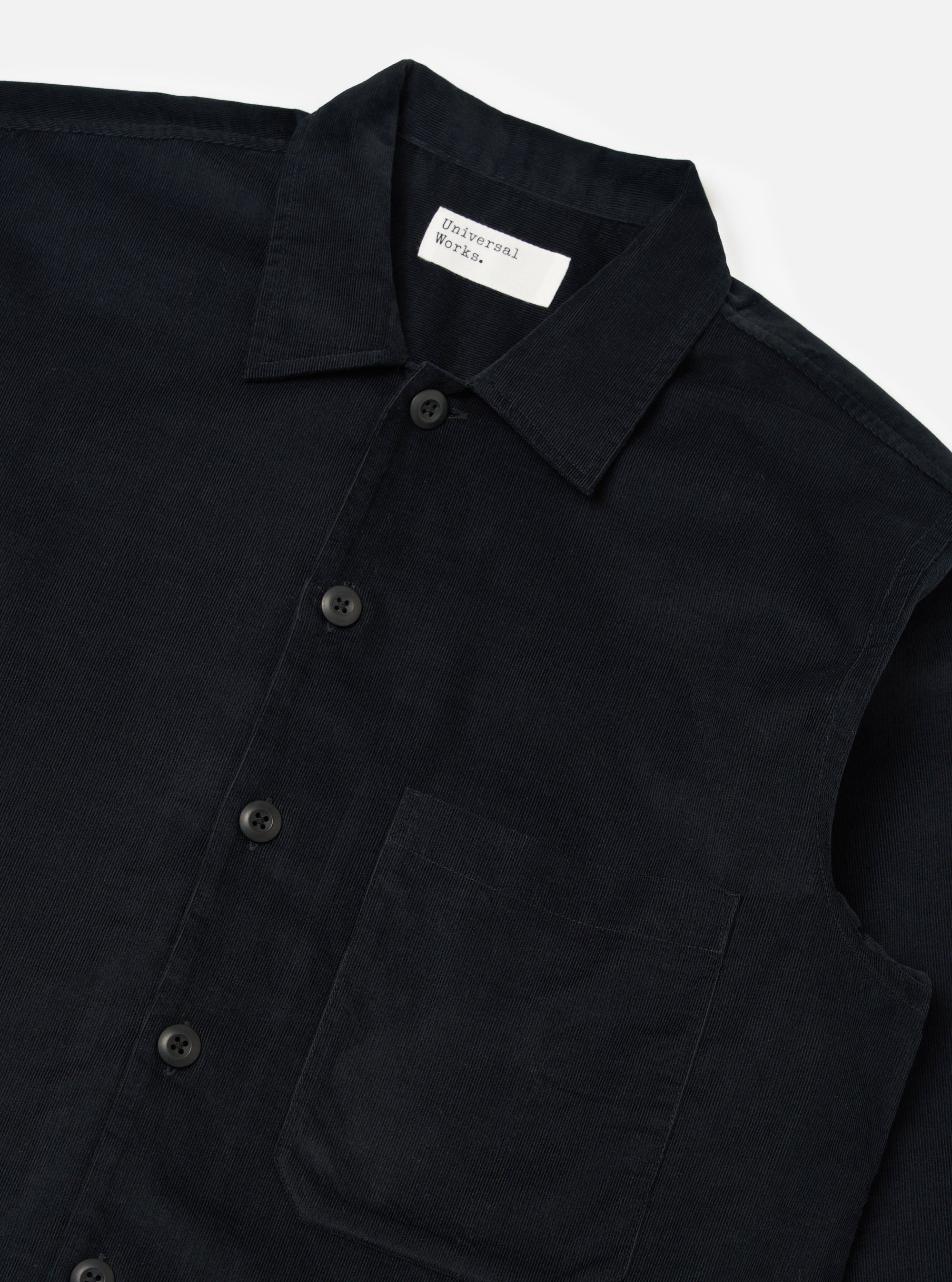 Close-up of the Black Organic Fine Cord Fatigue Shirt on a white surface. The shirt is dark, with visible corduroy texture, buttons, and a chest pocket.