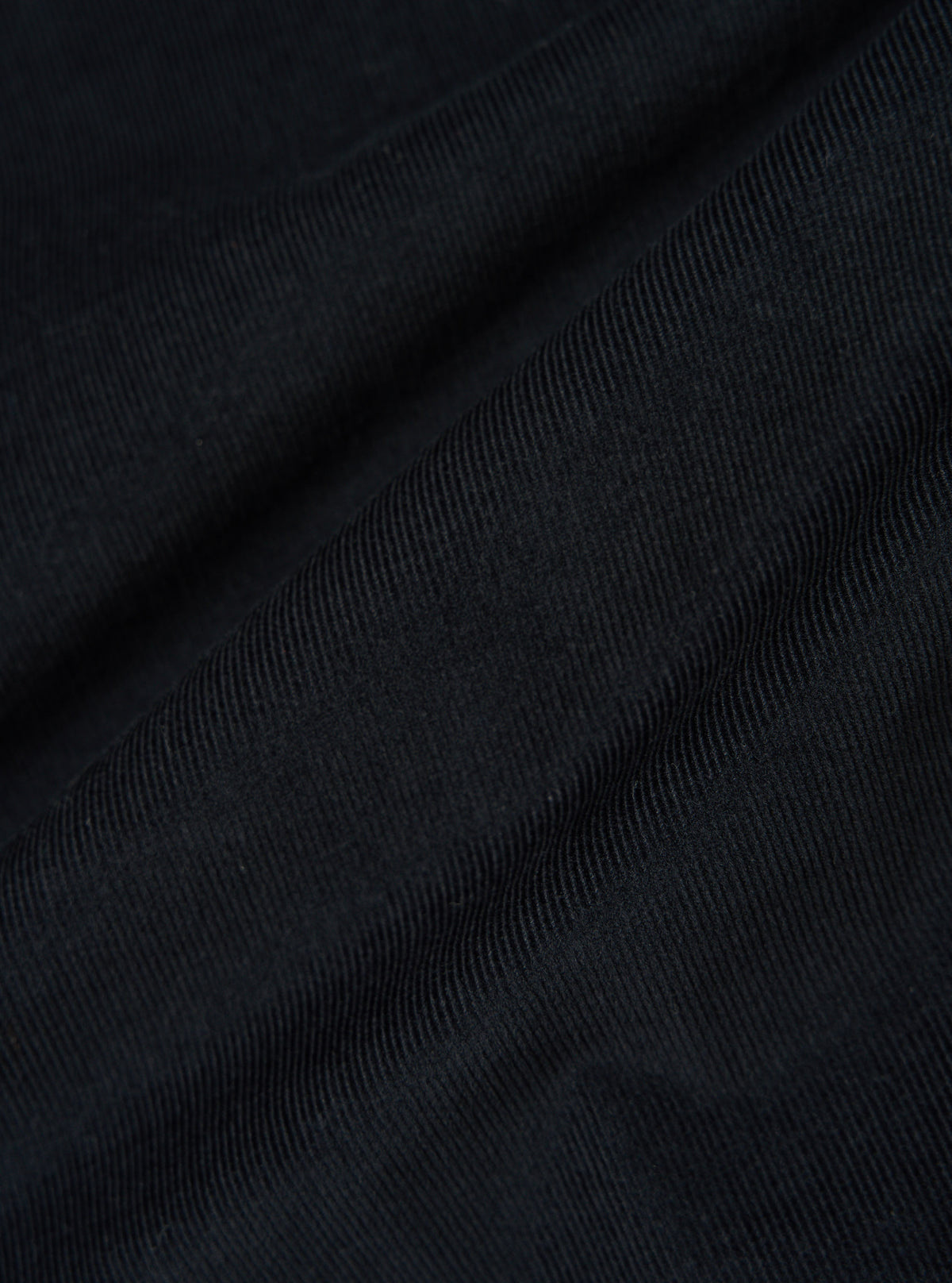 Close-up of the Black Organic Fine Cord Fatigue Shirt fabric. The fine cord texture is visible in the black material, draped on a flat surface.