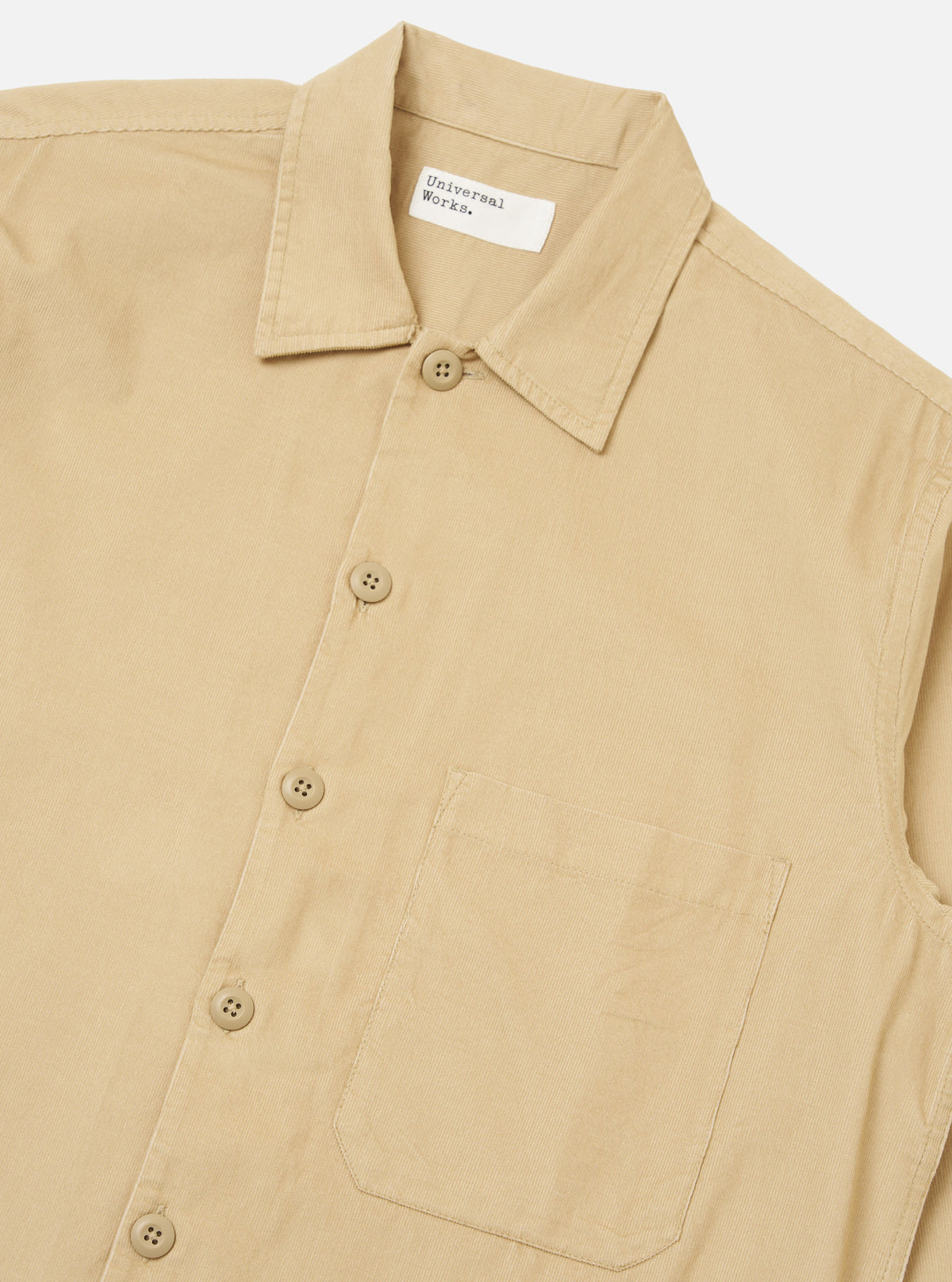 Close-up of the Sand Organic Fine Cord Fatigue Shirt. The shirt is a light tan color and made of fine corduroy. It features a button-down front and a chest pocket. The background is a plain white.