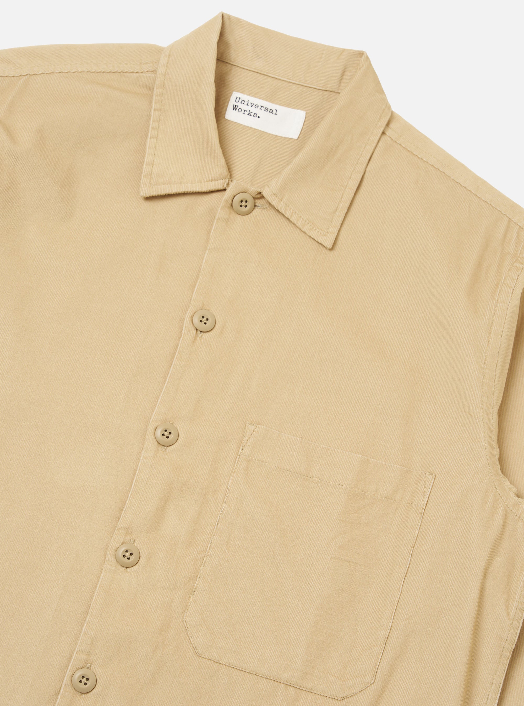Close-up of the Sand Organic Fine Cord Fatigue Shirt. The shirt is a light tan color and made of fine corduroy. It features a button-down front and a chest pocket. The background is a plain white.