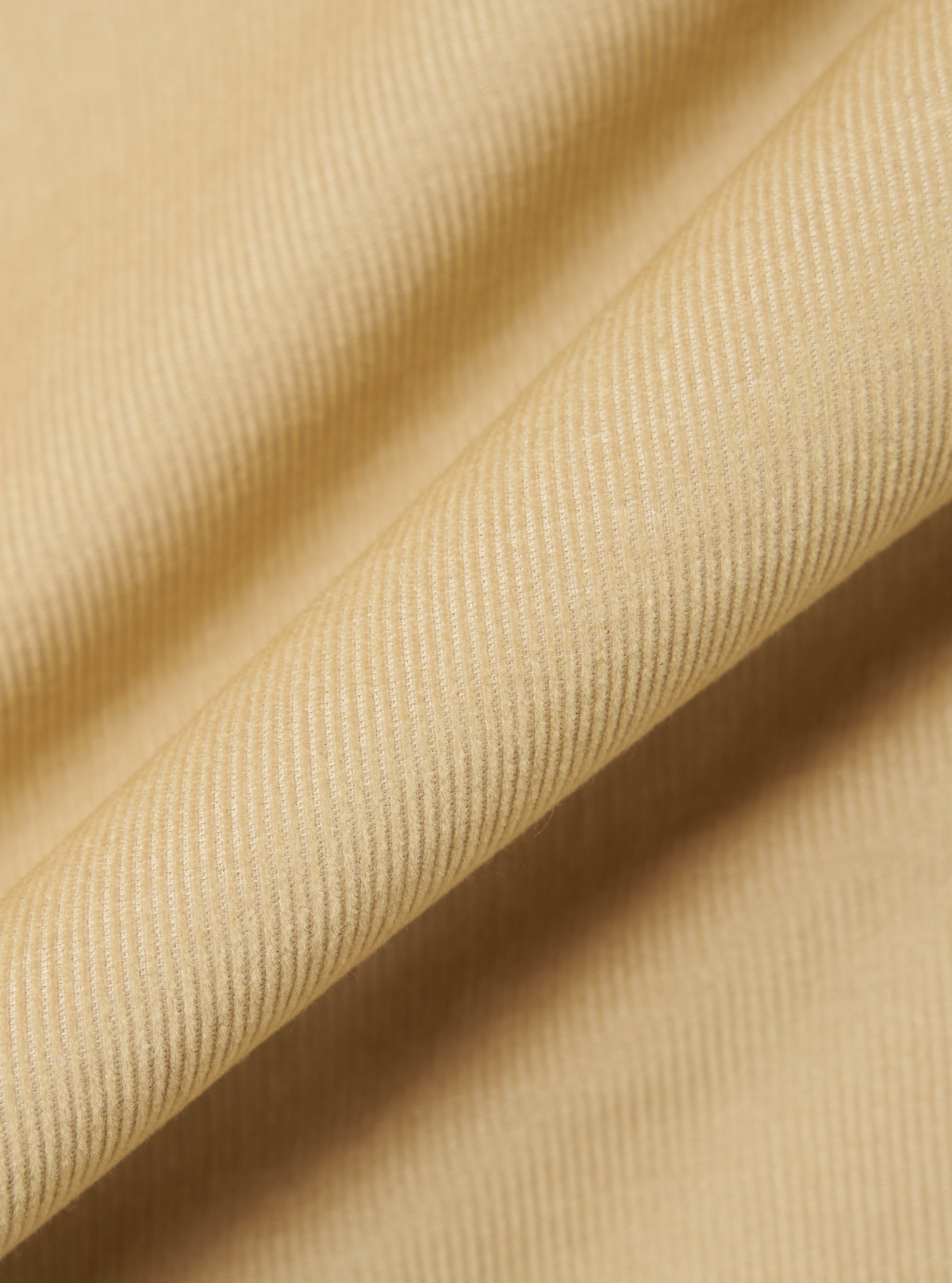 Close-up of the Sand Organic Fine Cord Fatigue Shirt fabric. The fine corduroy texture is visible in a soft, neutral sand color. The fabric is draped to show its texture.