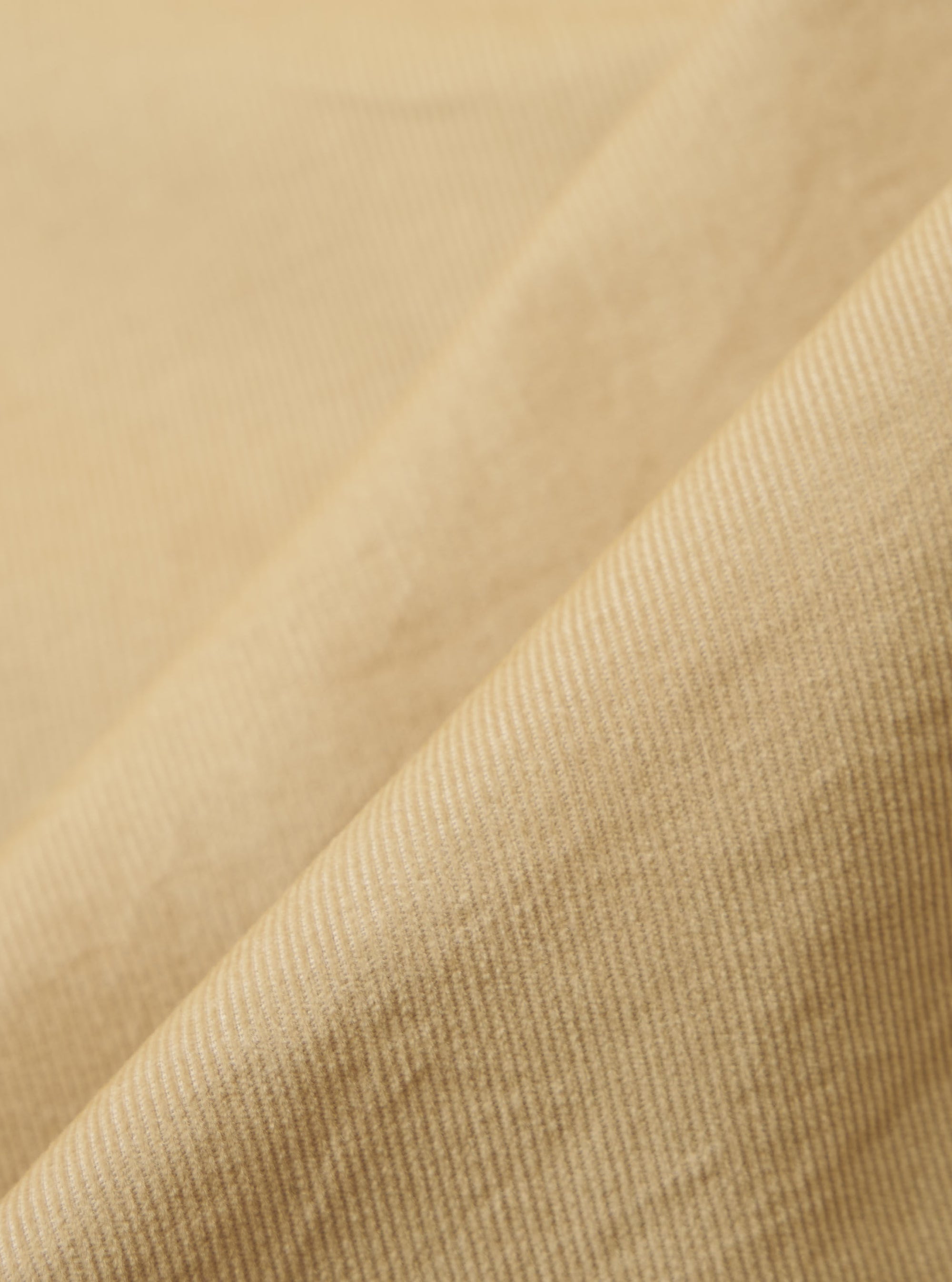 Close-up of the Sand Organic Fine Cord Daybrook Shirt fabric. The fine corduroy texture is visible in a soft, neutral sand color. The fabric is draped to show its texture.