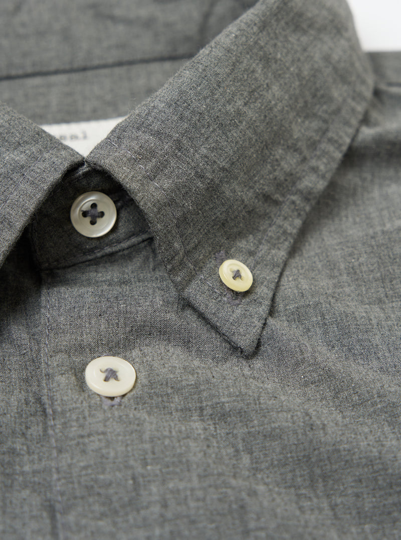 Close-up of the Charcoal Organic Chambray Patched Lazy Day Shirt collar. Shows the charcoal chambray fabric and button details. Shot on a white surface.