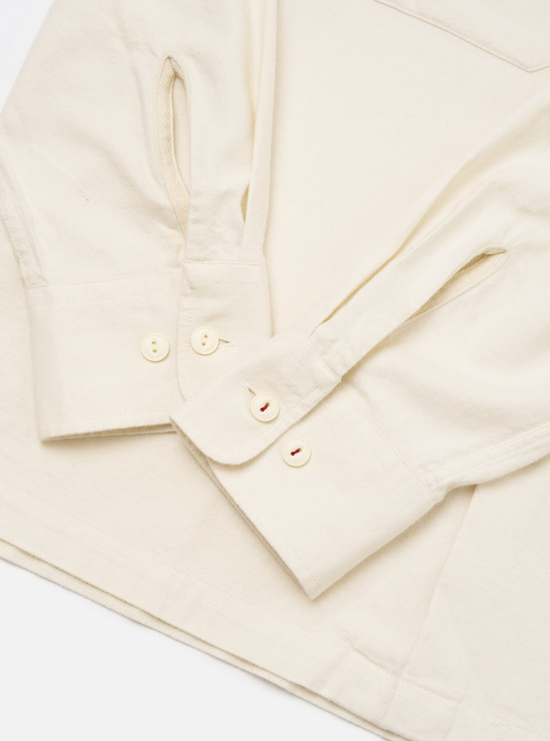 Close-up of the Ecru Sid Flannel CPO Shirt on a white surface. Shows the ecru flannel material, buttoned cuffs, and red stitching detail on the buttons.