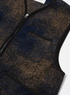 Close-up of the Navy Deca Check Zip Gilet on a white surface. The gilet features a blue and brown check pattern, a zip-up front, and a chest pocket.