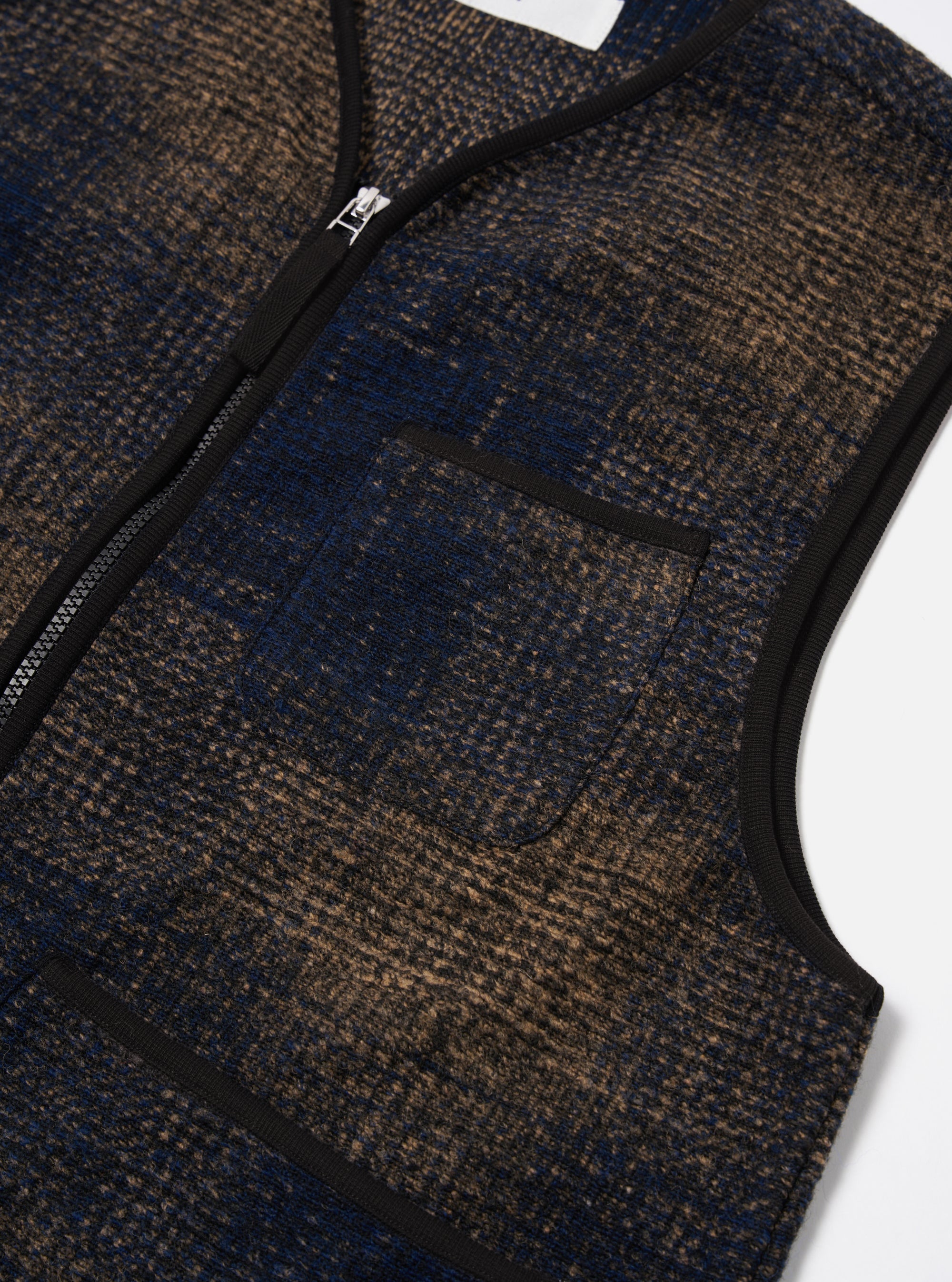 Close-up of the Navy Deca Check Zip Gilet on a white surface. The gilet features a blue and brown check pattern, a zip-up front, and a chest pocket.