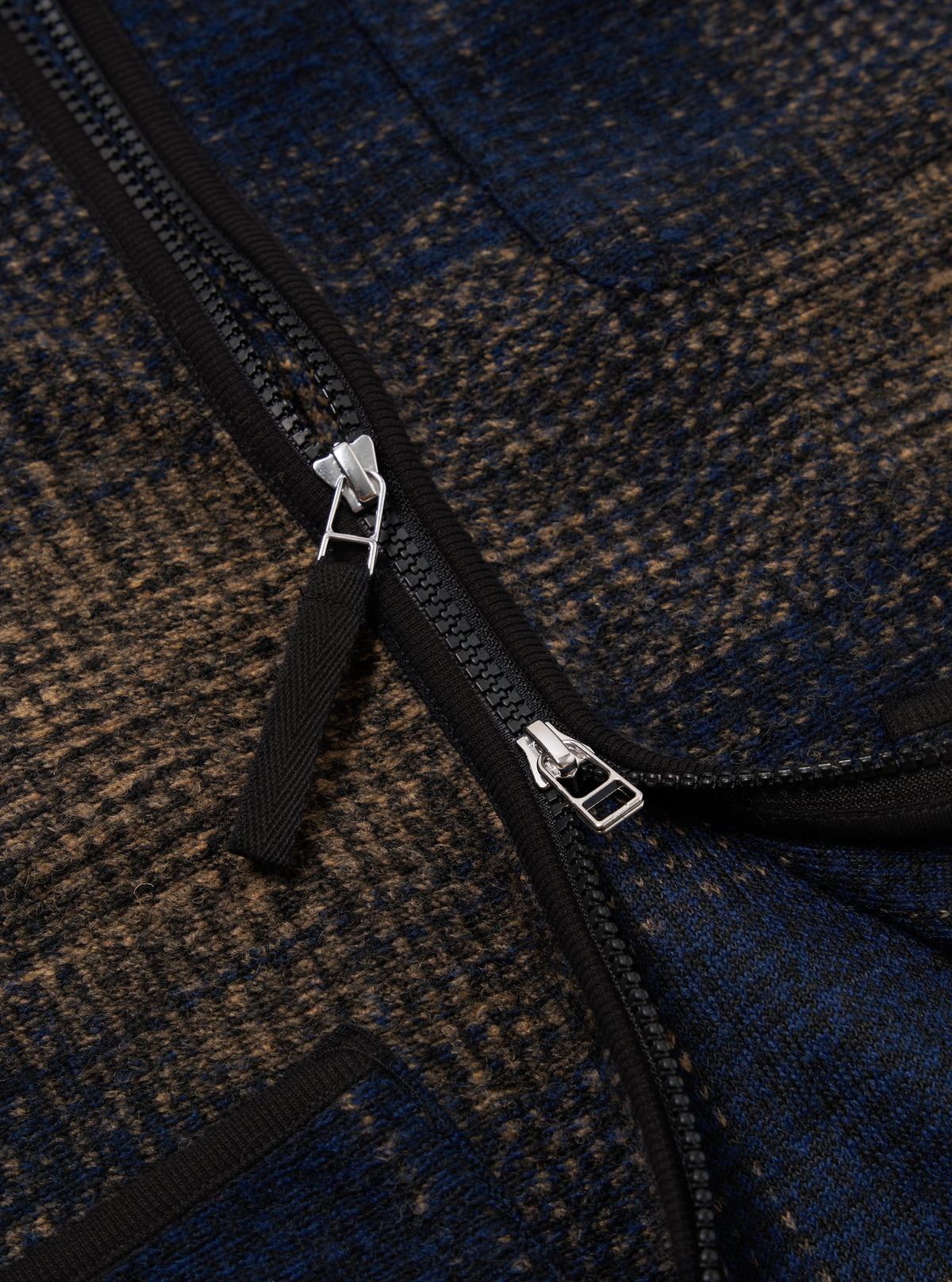 Close-up of the Navy Deca Check Zip Gilet, showcasing its blue and brown checked pattern and black zipper. The image is tightly cropped to highlight the texture and detail.