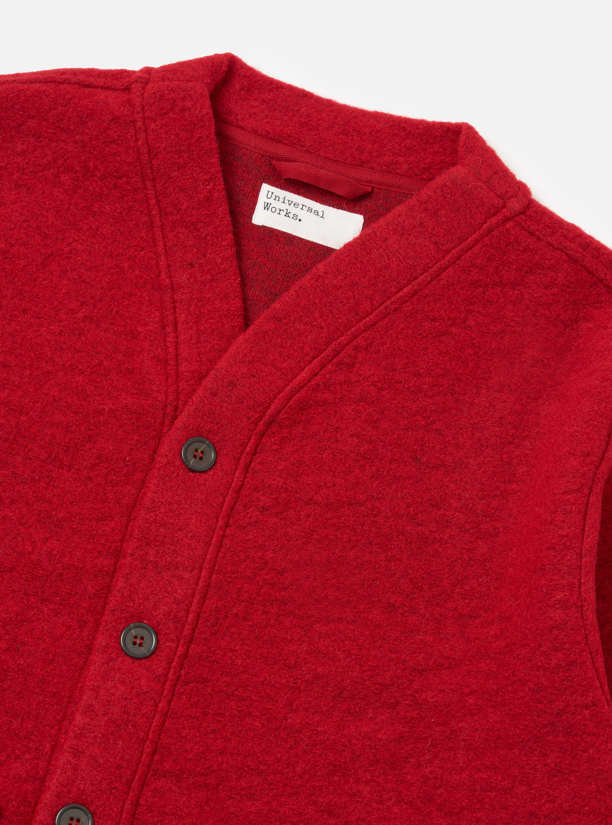 Close up of the Red Wool Fleece Advance Cardigan, a vibrant red wool cardigan with dark buttons, laid flat on a white surface.