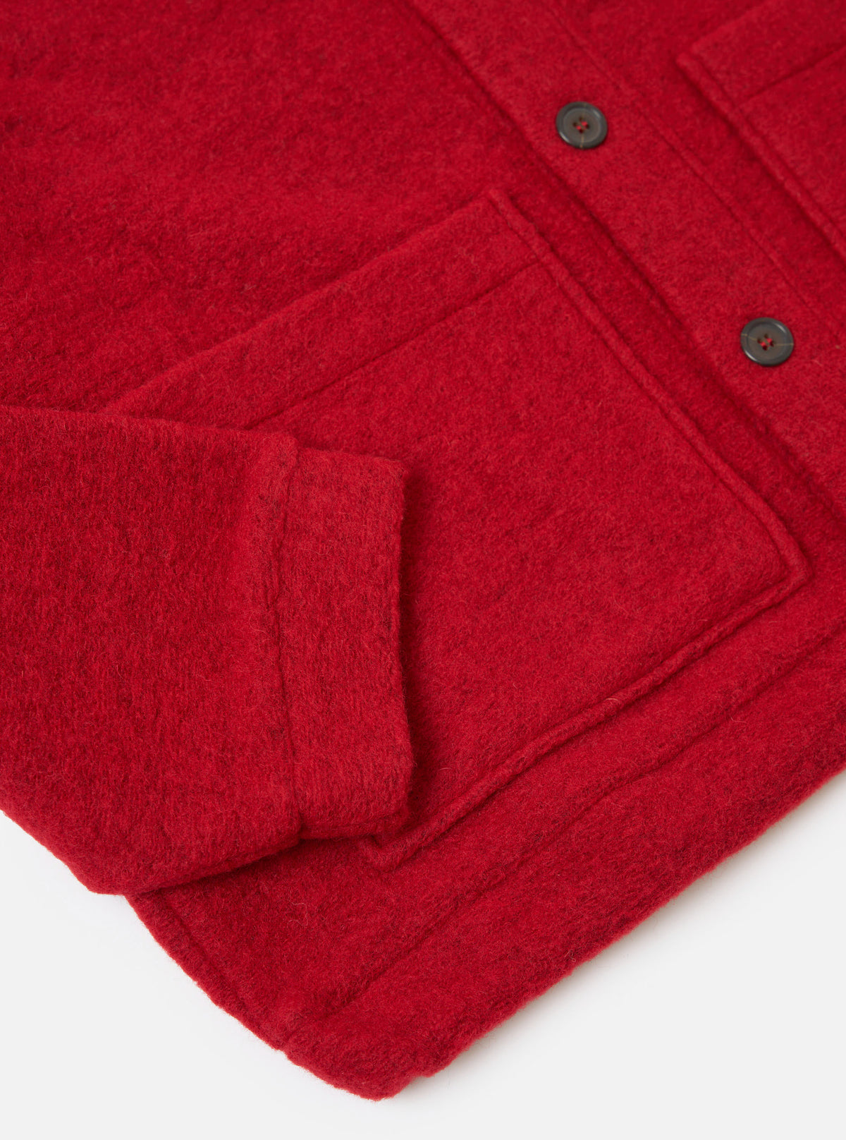 Close-up of the Red Wool Fleece Advance Cardigan on a white surface, showing the texture, pocket, sleeve, and buttons.
