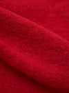 Close-up of the red wool fleece advance cardigan, showing the texture and color of the fabric. The background is a plain surface.