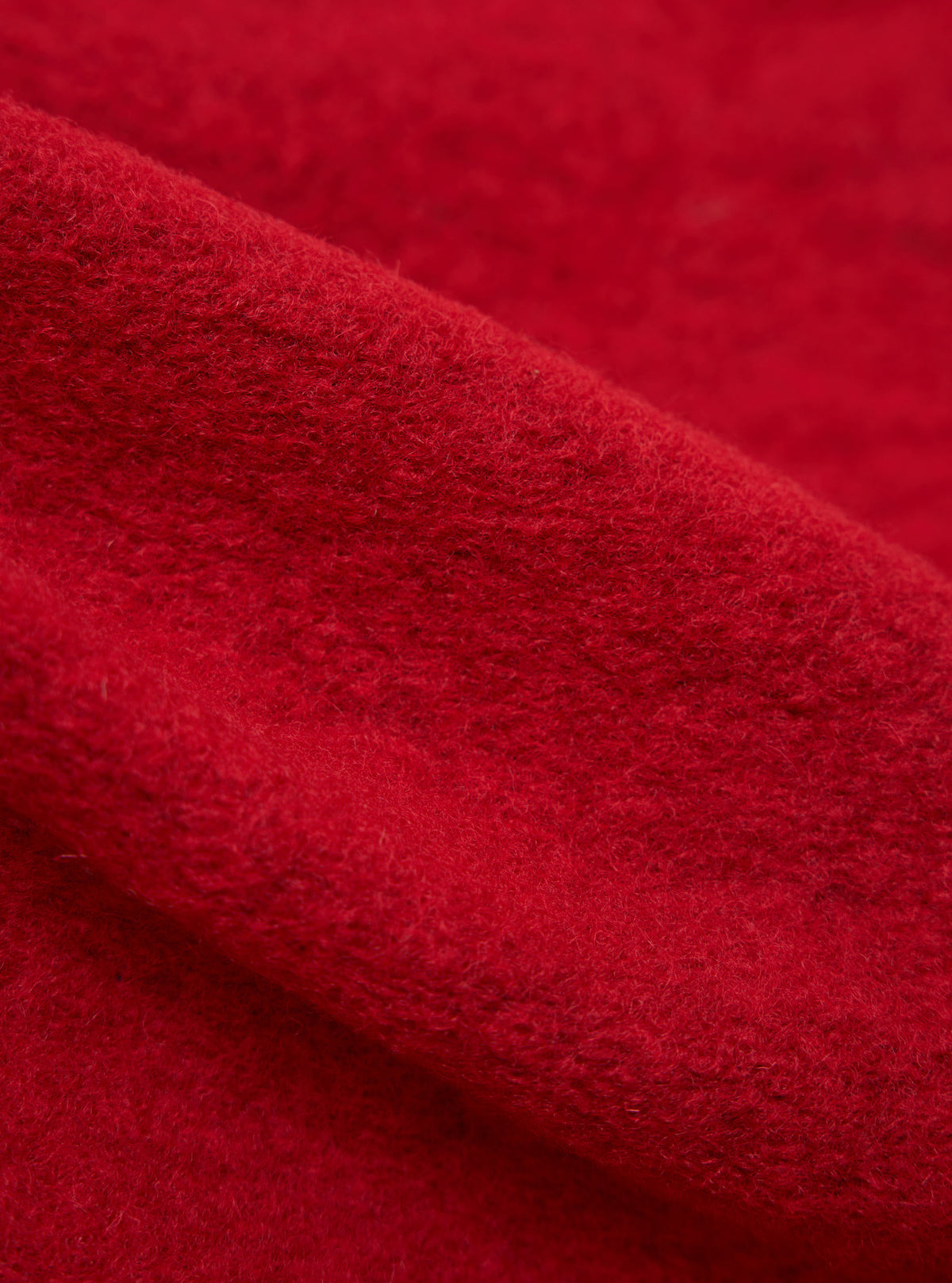 Close-up of the red wool fleece advance cardigan, showing the texture and color of the fabric. The background is a plain surface.