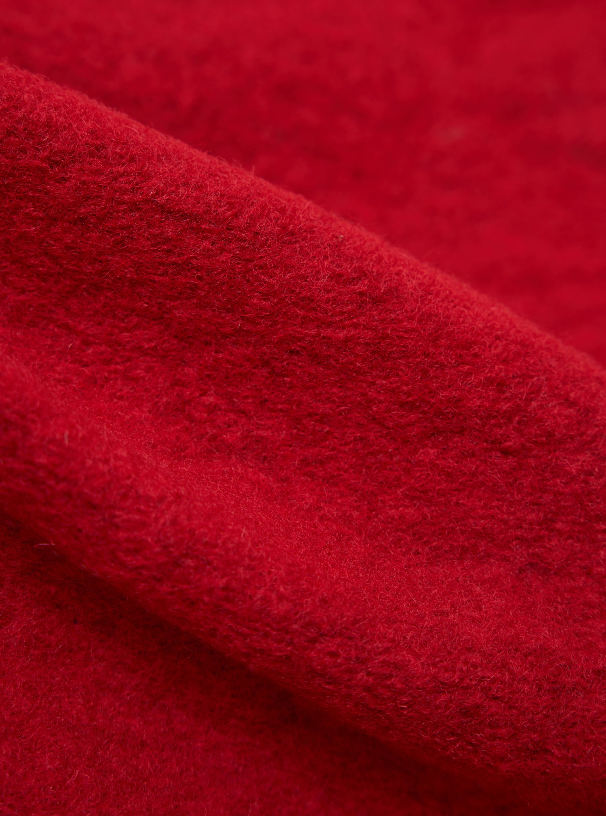 Close-up of the red wool fleece advance cardigan, showing the texture and color of the fabric. The background is a plain surface.