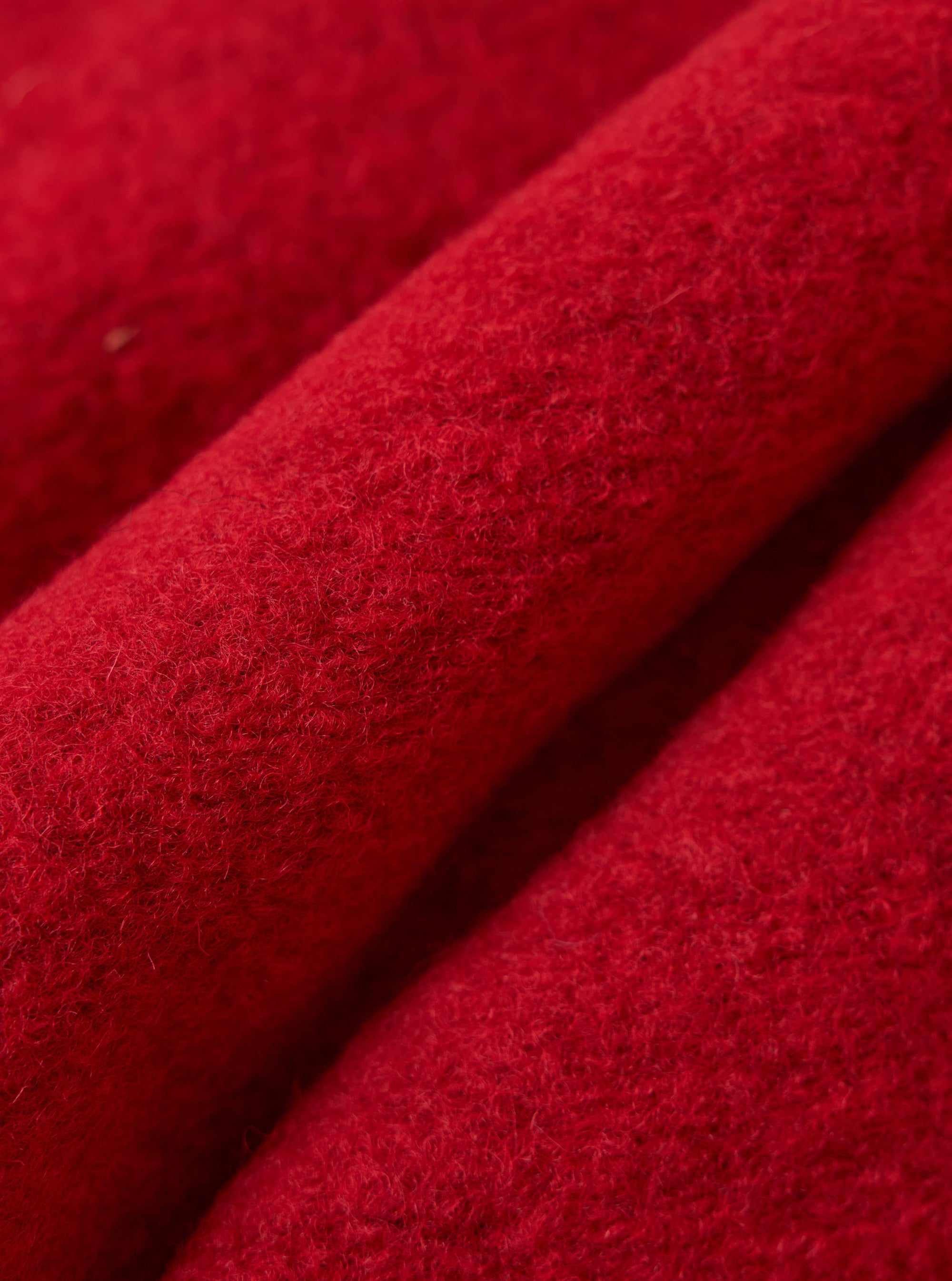Close-up of the Red Wool Fleece Rams Jacket. The bright red wool material is folded, showing the texture of the fleece. 