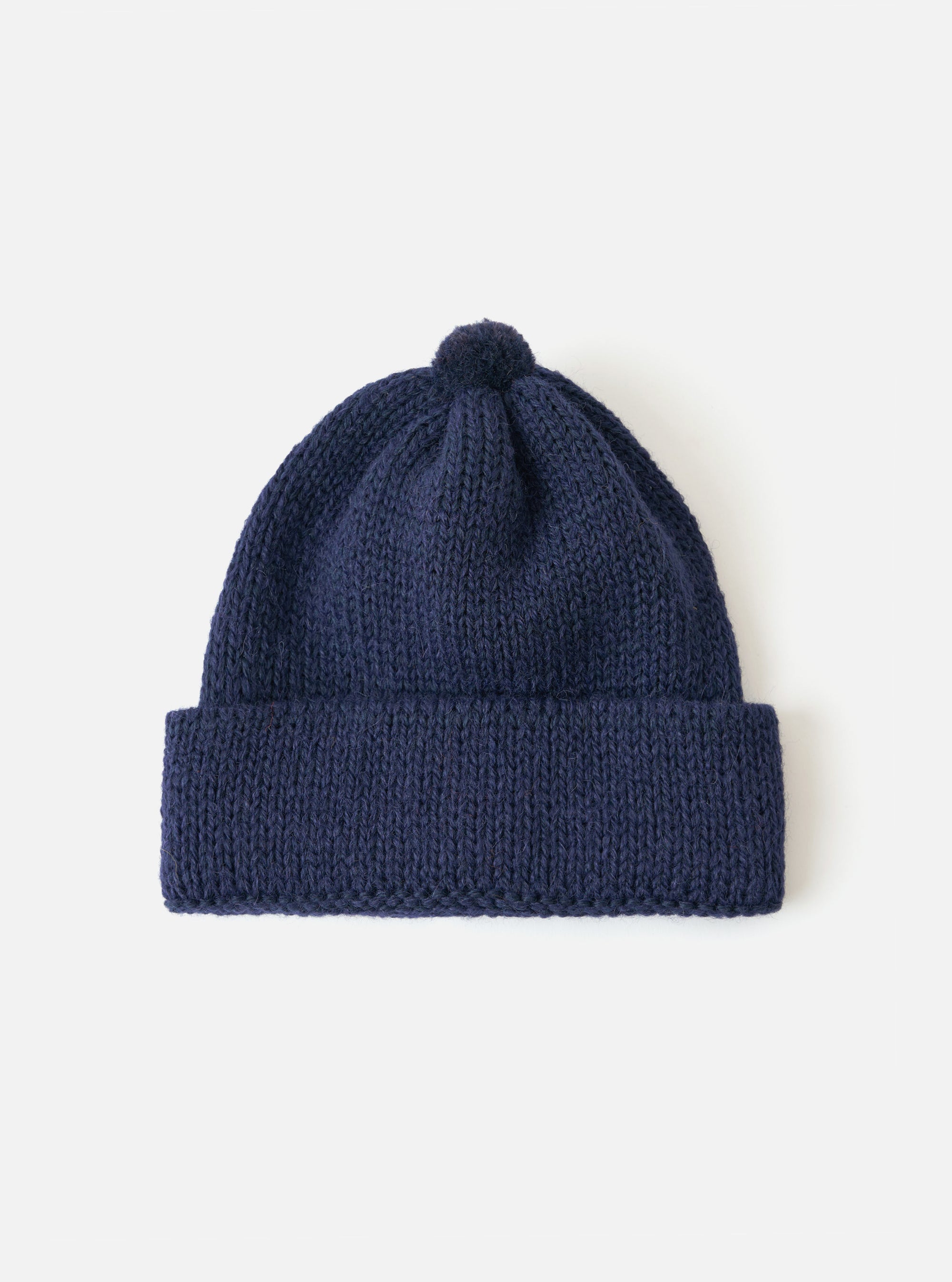Close-up of a Navy Alpaca/British Wool Bobble Hat on a white background. The knitted hat has a folded brim and a bobble on top.