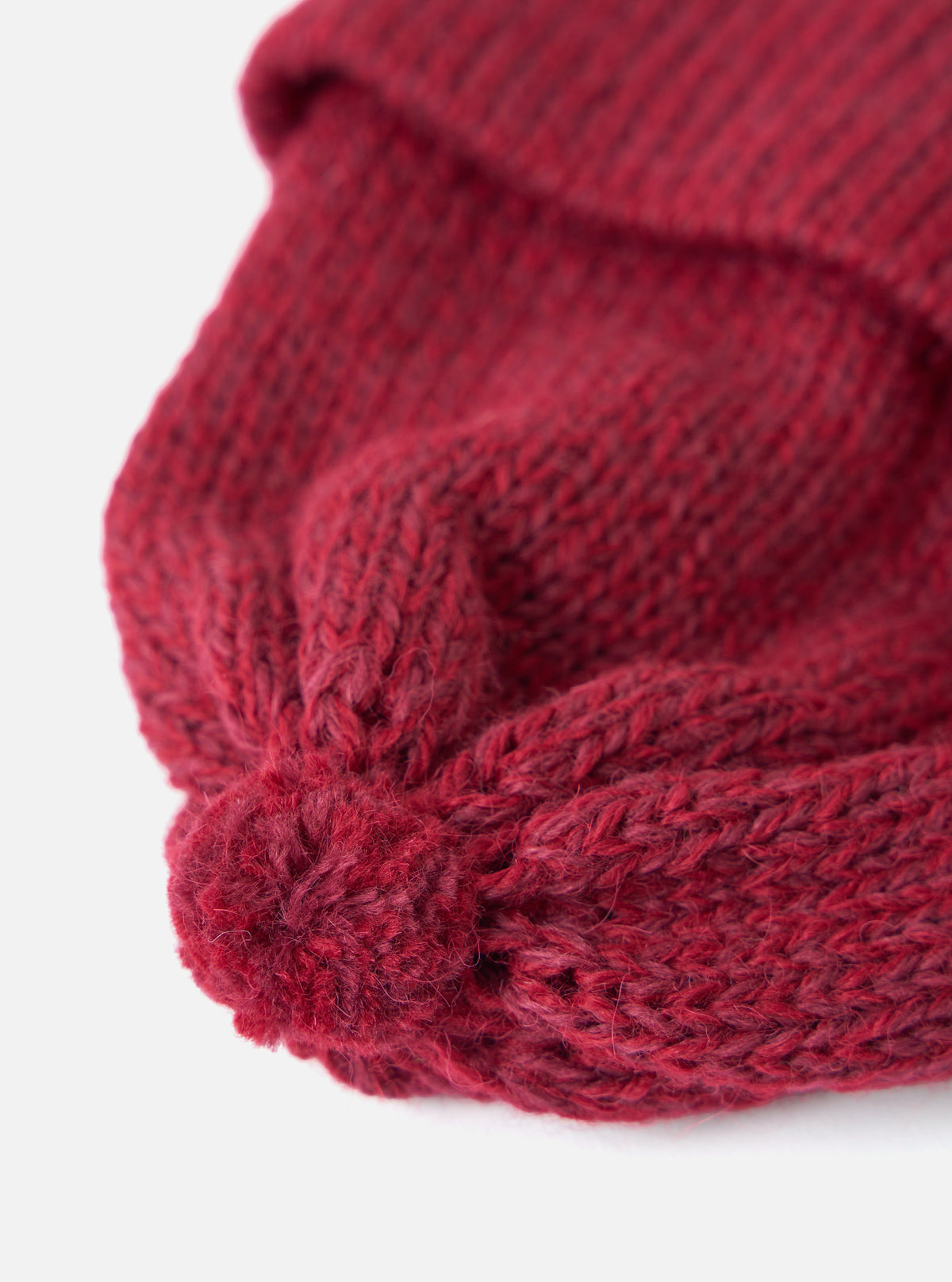 Close-up of a red Alpaca/British Wool Bobble Hat on a white background. The knitted texture and bobble detail are clearly visible.