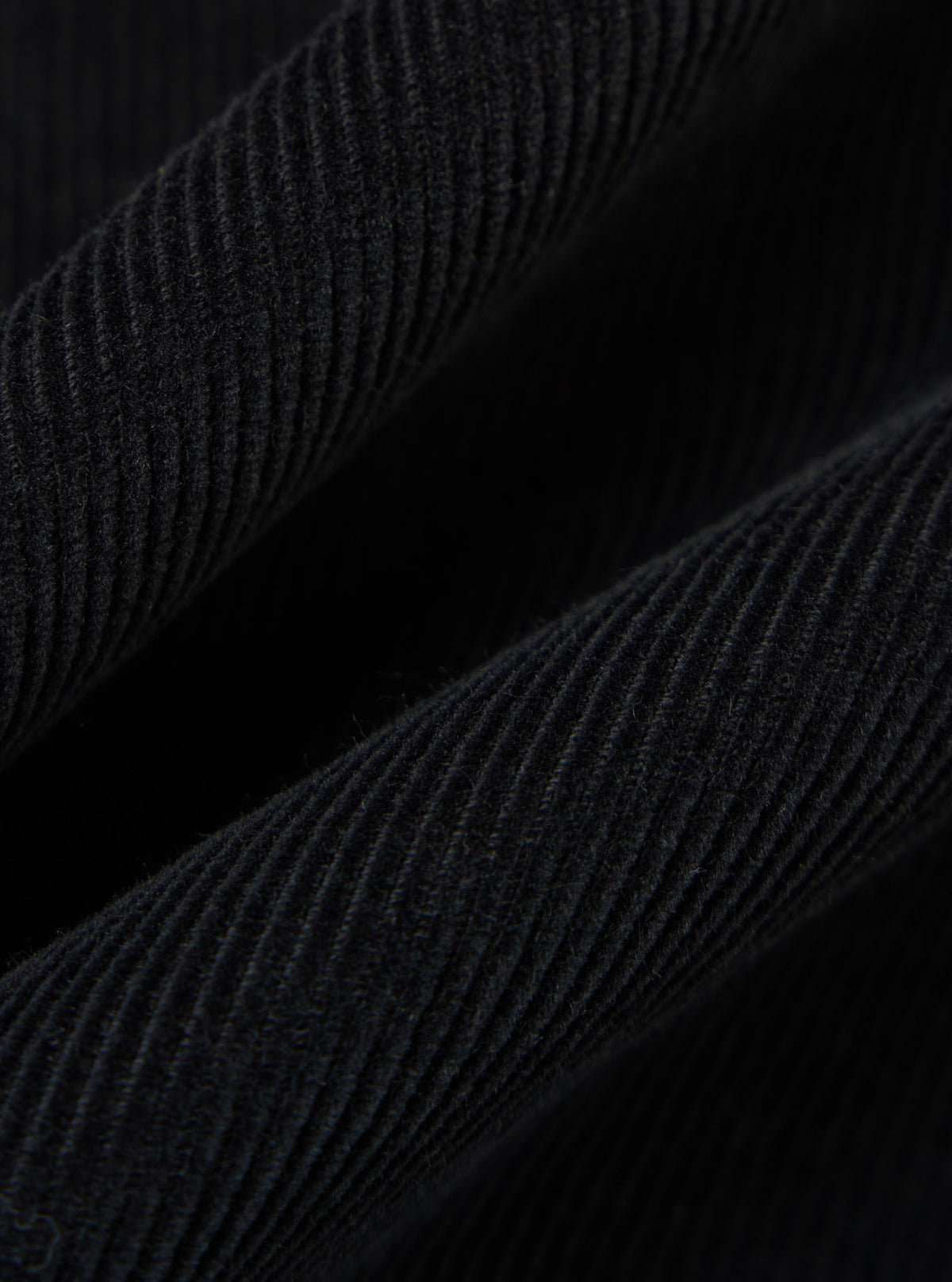 Close-up of the Black Cat Cord Two Button Jacket, showcasing the texture and detail of the black corduroy fabric. The jacket is draped against a dark background.