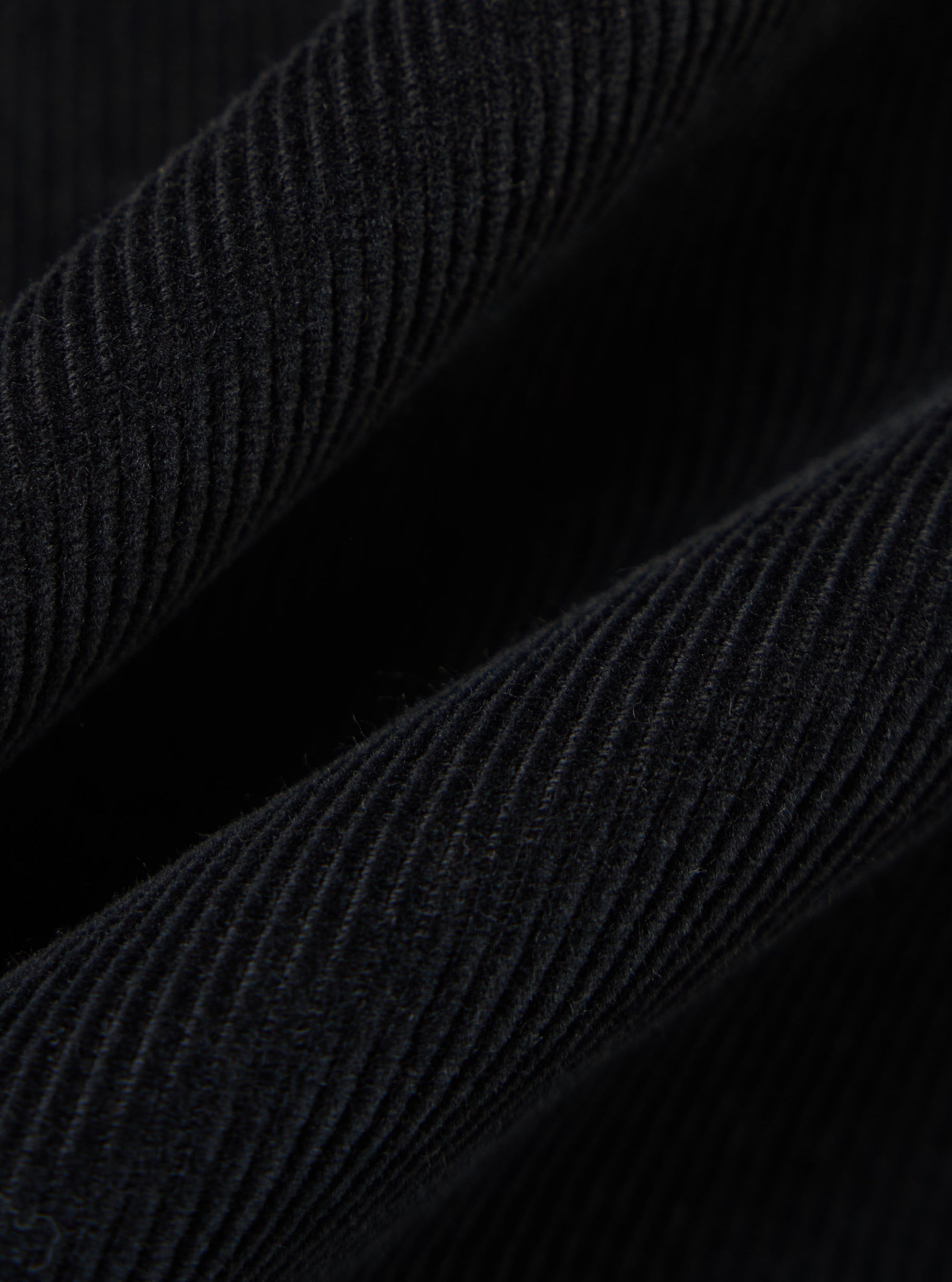 Close-up of the Black Cat Cord Two Button Jacket, showcasing the texture and detail of the black corduroy fabric. The jacket is draped against a dark background.